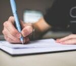 Close-up of hand writing in notebook using a blue pen, focus on creativity.